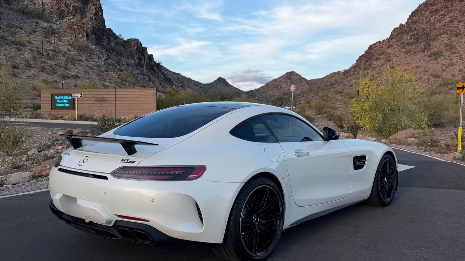 A white Mercedes-AMG GT parked among Arizona desert mountains, newly listed for rent